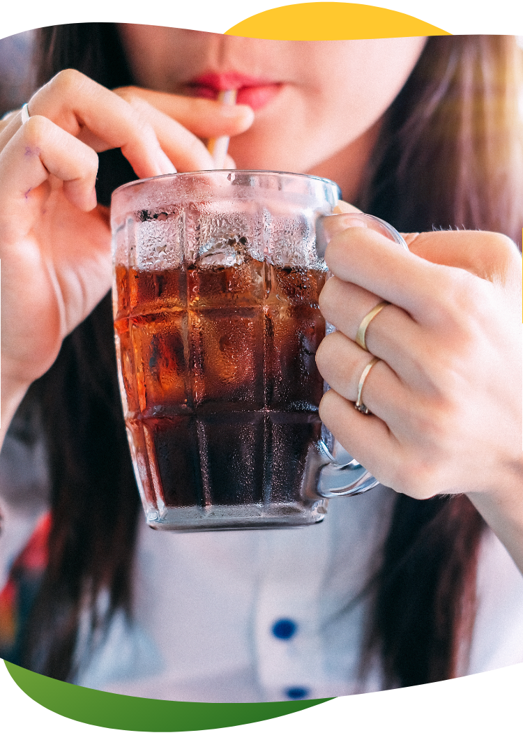 A young woman with long, brown hair holds a tall glass with her hand and drinks a carbonated drink with a straw out of it